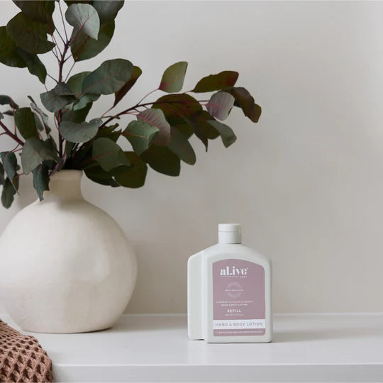 White bottle of aLive product on a white surface with a vase and eucalyptus leaves in the background.
