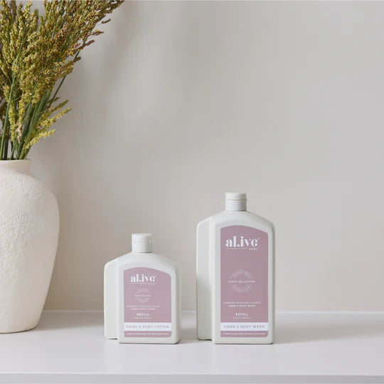 Two bottles of 'alive' skincare products on a white surface with a vase of flowers in the background.