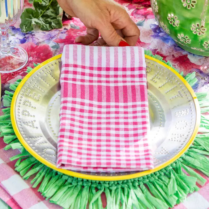 Pink and white checkered napkin on a decorative plate with a colorful tablecloth in the background