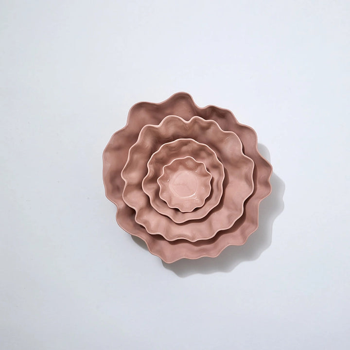 Set of three pink ceramic bowls with wavy edges on a light gray background