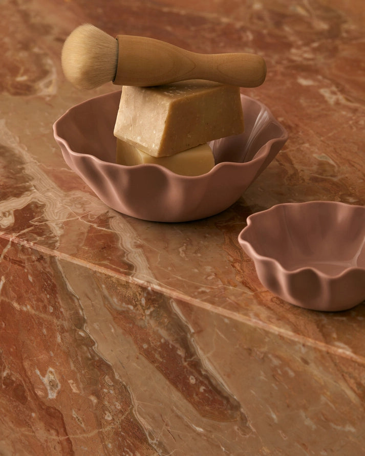 Pink ceramic dish with soap and brush on a marble surface