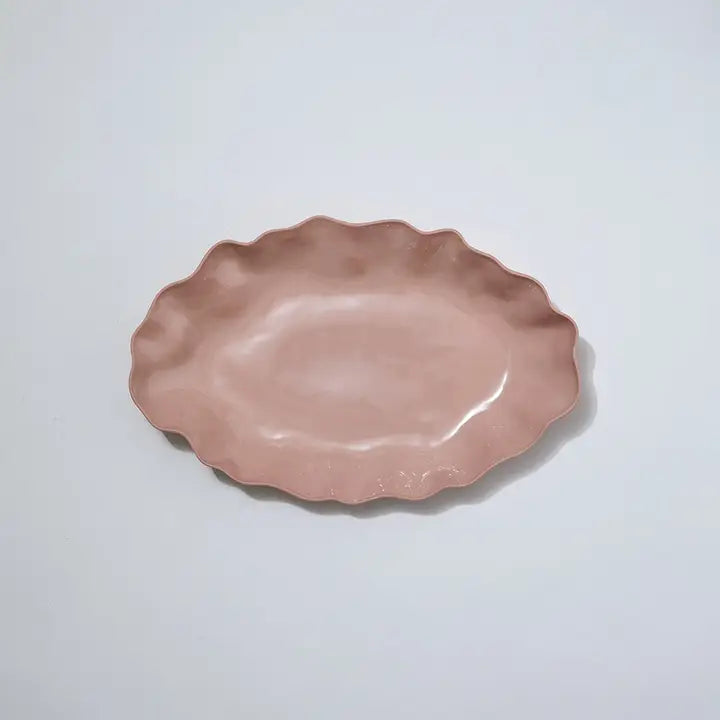Pink ceramic dish with scalloped edge on a light gray background