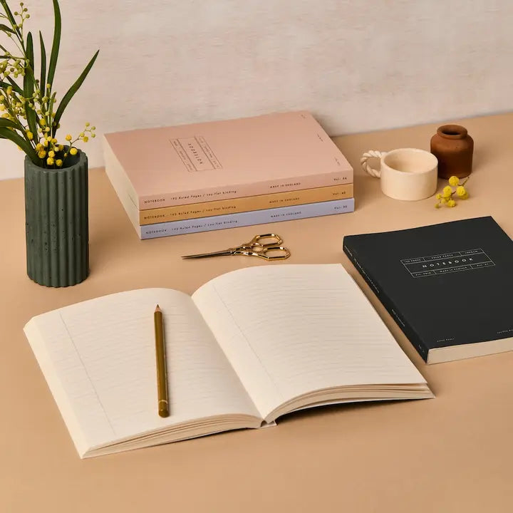 Open notebook with a pen on a table with books and decorative items.