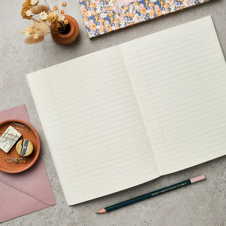 Open notebook with lined pages on a gray surface, surrounded by stationery items.