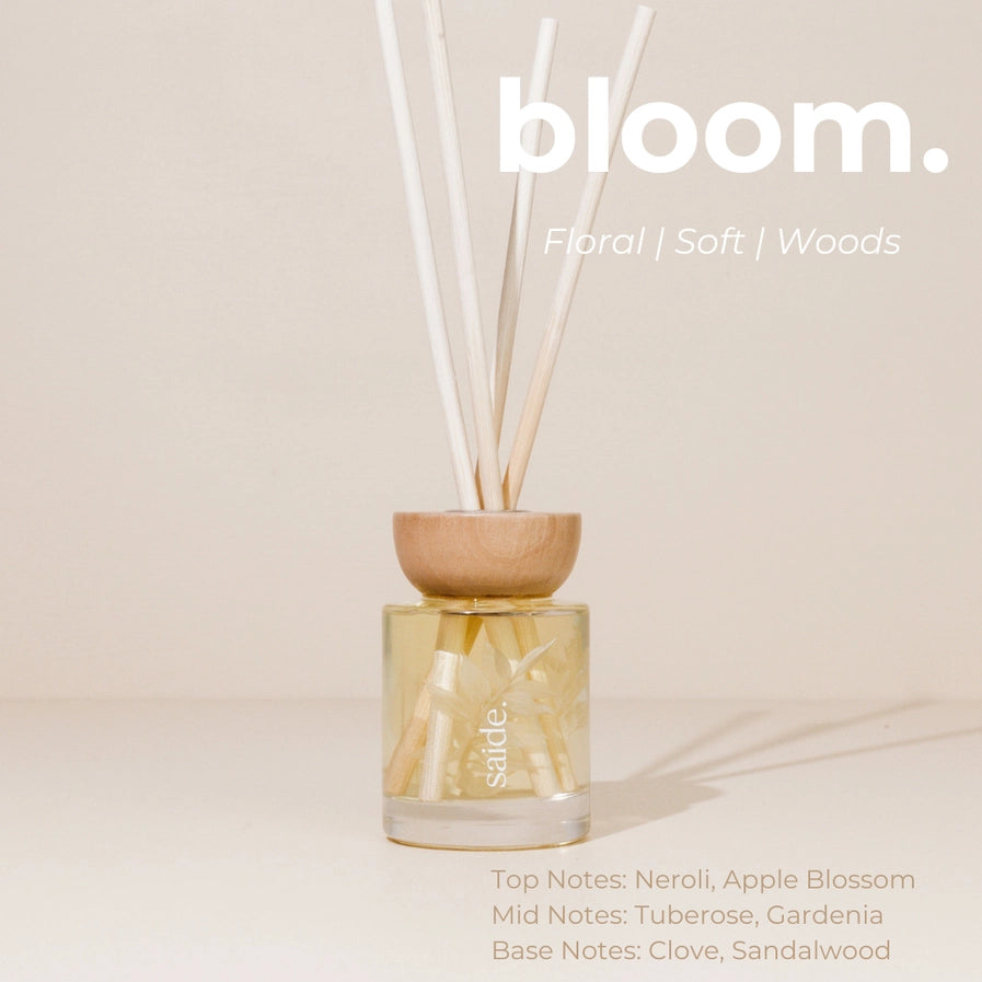 A diffuser with wooden top and glass container on a beige background, featuring the brand 'bloom'.