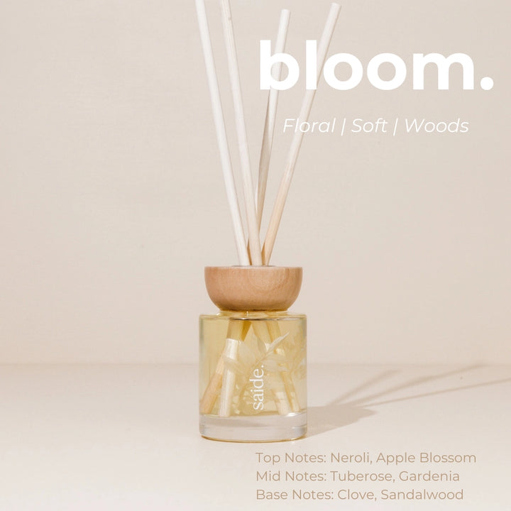A diffuser with wooden top and glass container on a beige background, featuring the brand 'bloom'.