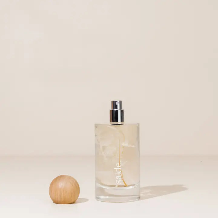Clear glass bottle with silver cap and wooden sphere on beige background