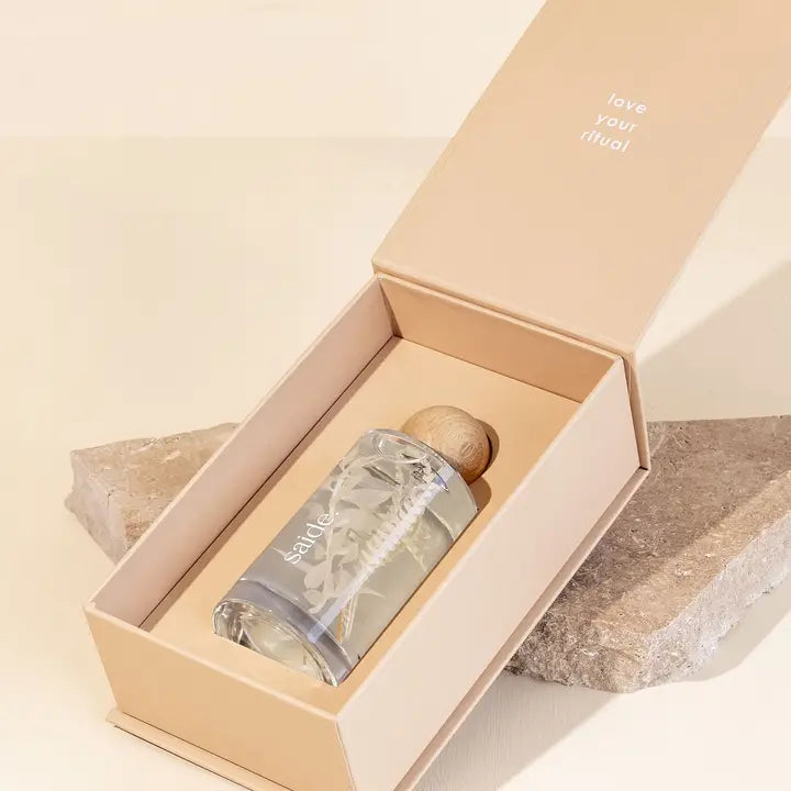 Clear glass interior fragrance bottle with wooden cap in a beige box on a stone surface