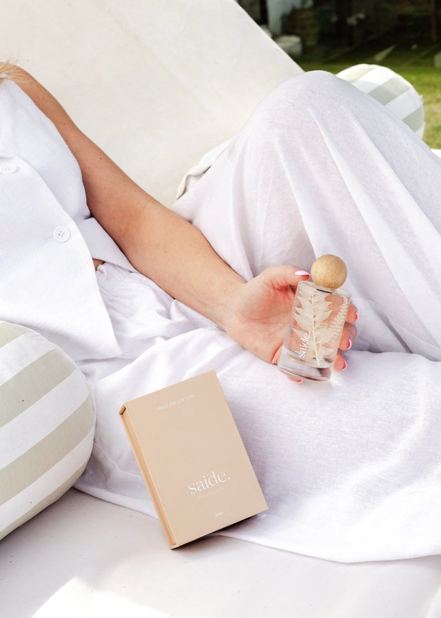 Person holding an interior fragrance bottle and a book on a white blanket outdoors