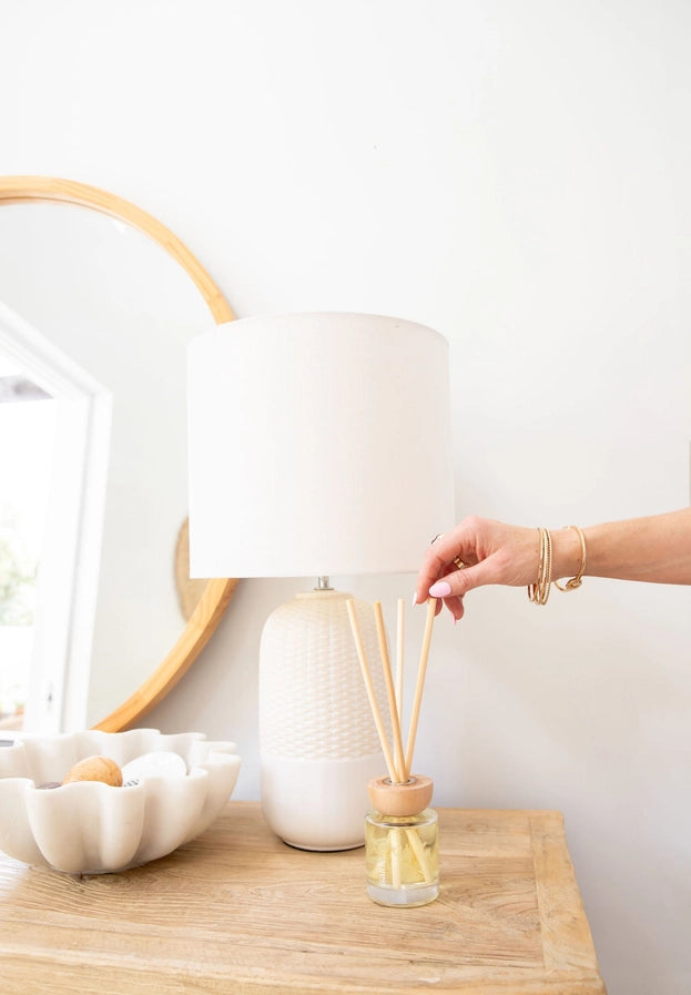 Person holding a diffuser on a wooden table with decorative items.
