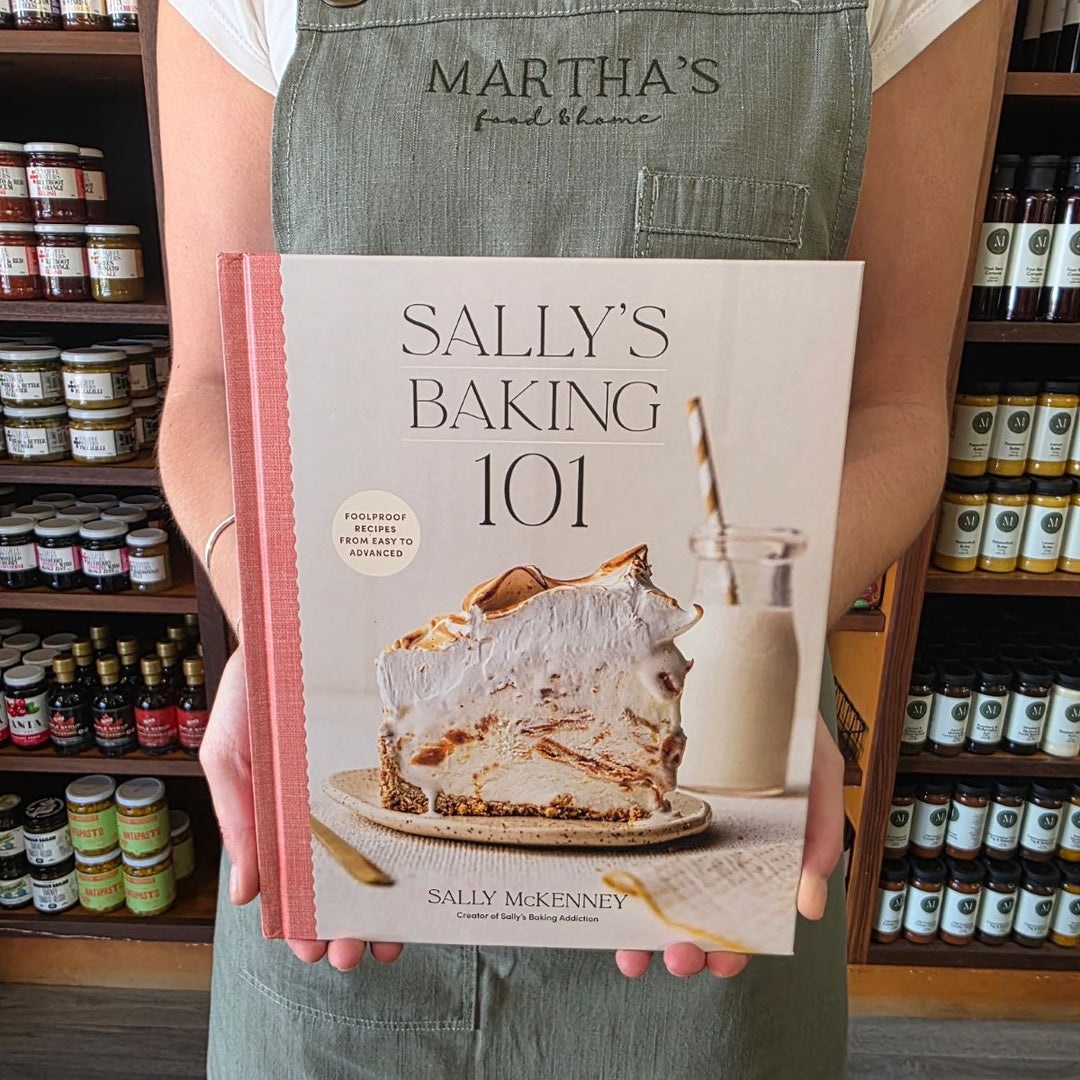 Person holding a baking book titled 'Sally's Baking 101' in a store setting.