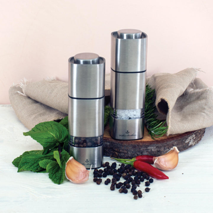 Two silver salt and pepper shakers on a wooden tray with herbs and spices on a light background