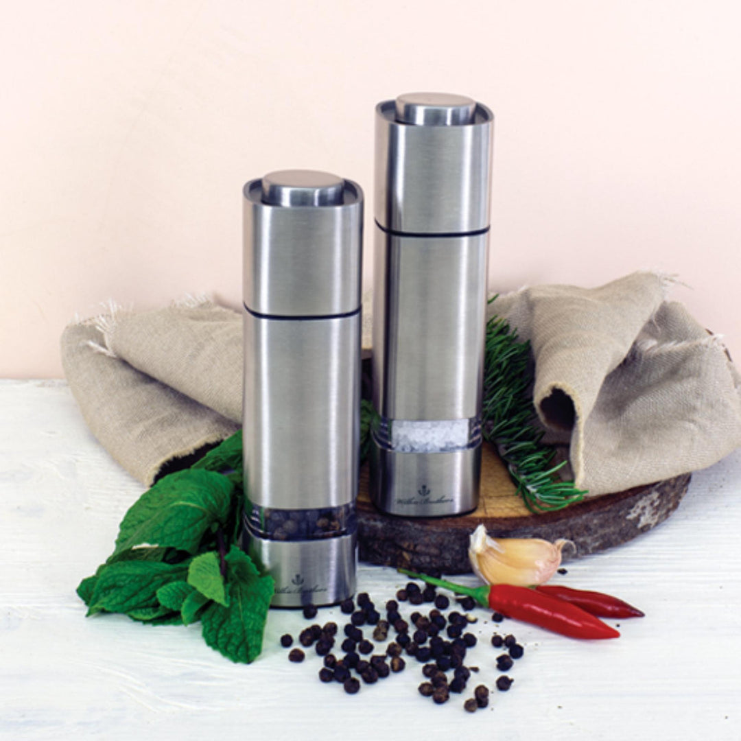 Two silver salt and pepper shakers on a wooden board with herbs and spices.