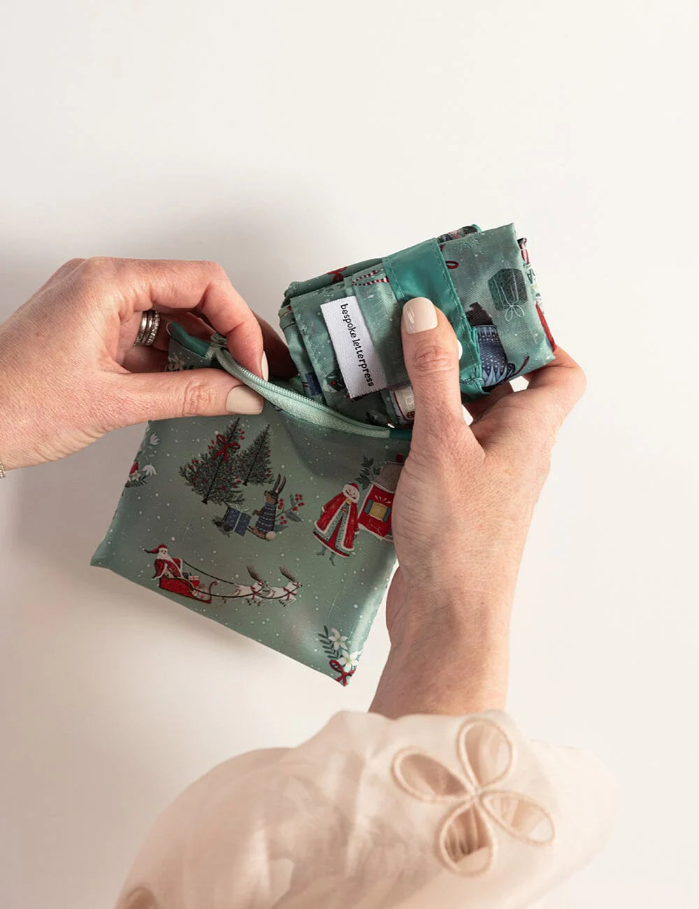 Person holding a green fabric pouch with Christmas design on a white background