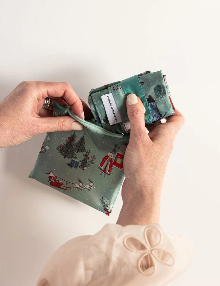 Person holding a green fabric pouch with Christmas design on a white background