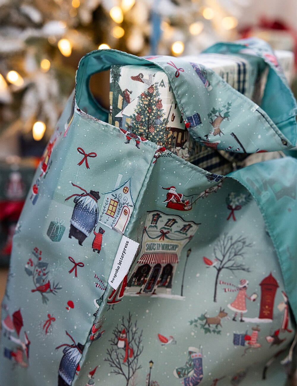 Gift bag with Christmas-themed design in front of a blurred Christmas tree.
