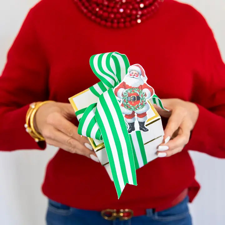 Person holding a Christmas-themed gift box with Santa Claus design and green ribbon.