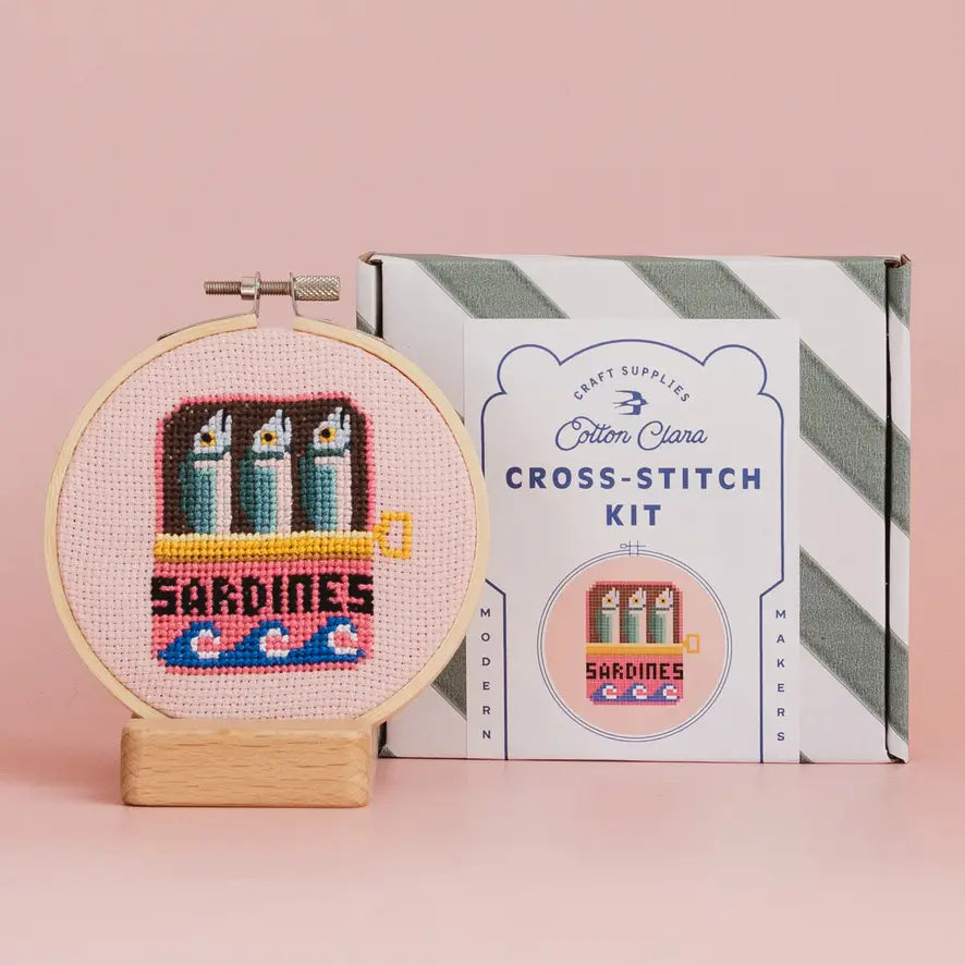 Cross-stitch kit with 'Sardines' design and Cotton Clara packaging on a pink background