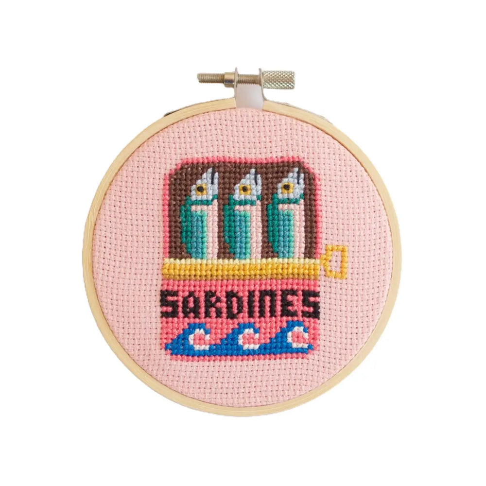 Cross-stitched design of sardines in a can on a pink background with 'Sardines' text.