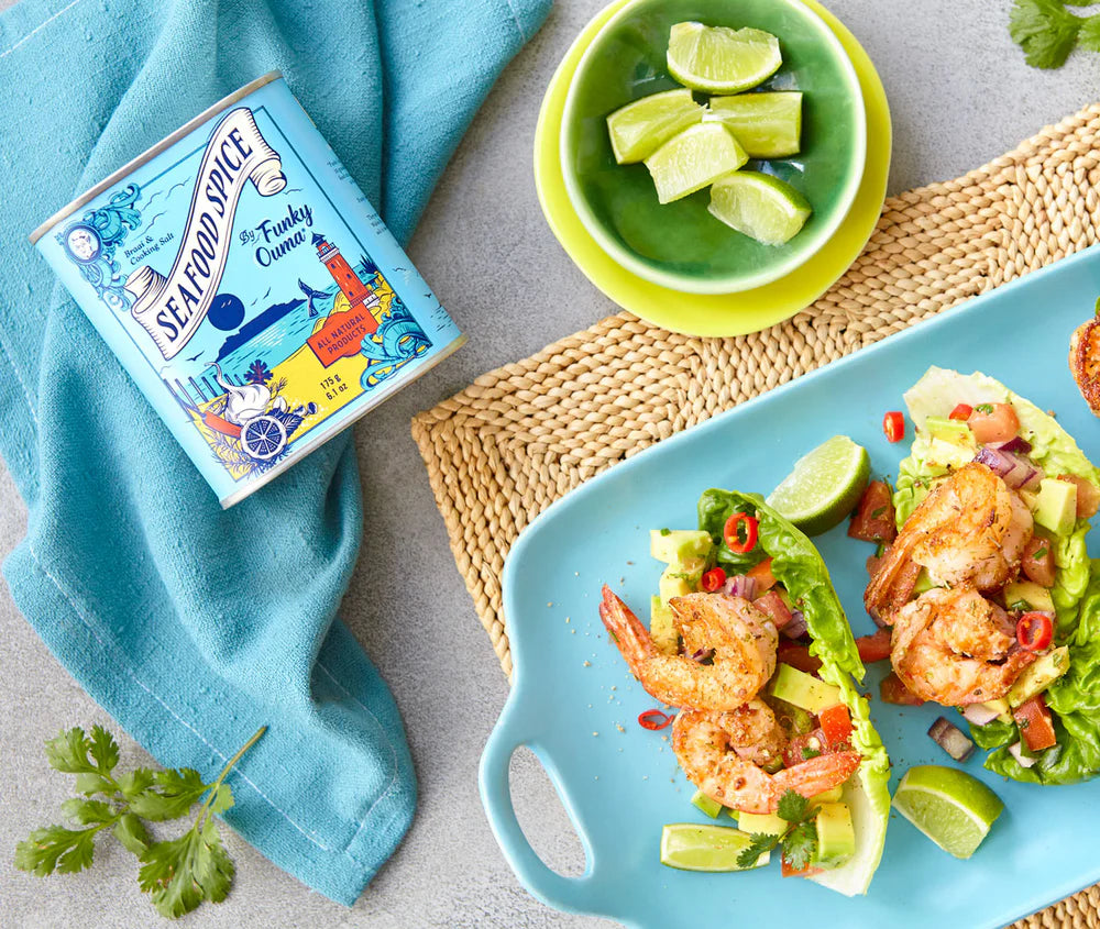 Plated shrimp salad with a box of Seafood Spice and lime wedges on a textured surface.