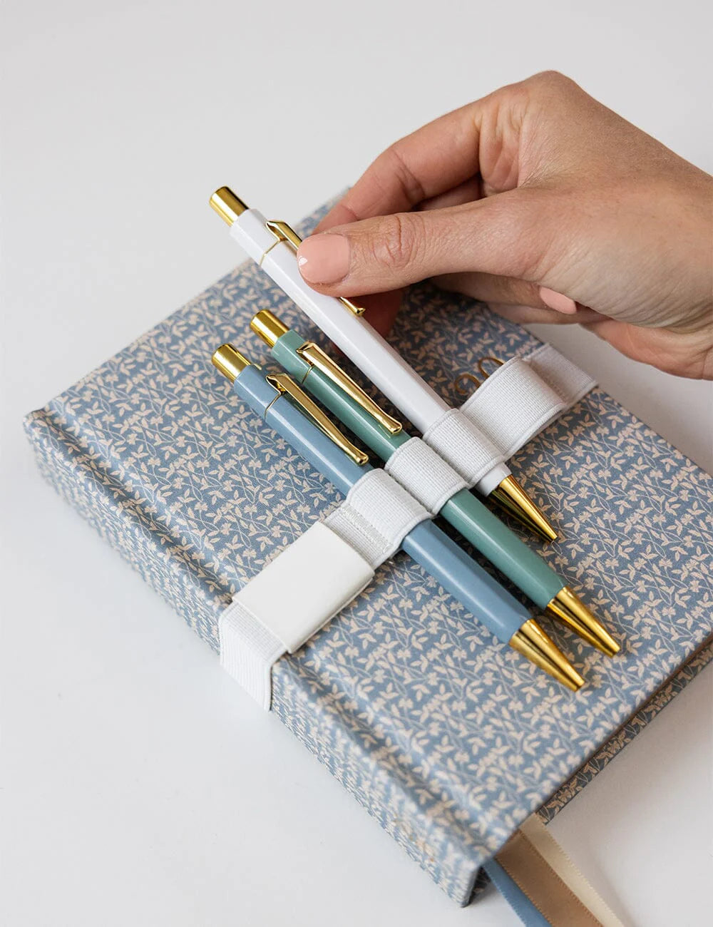 Hand holding a set of pens over a patterned notebook