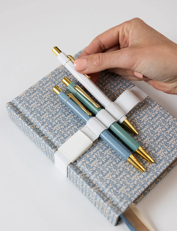 Hand holding a set of pens over a patterned notebook