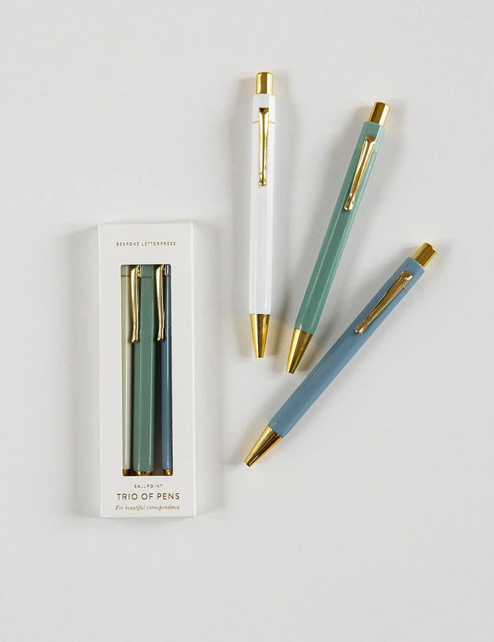 Set of three pens with gold accents and packaging on a light gray background