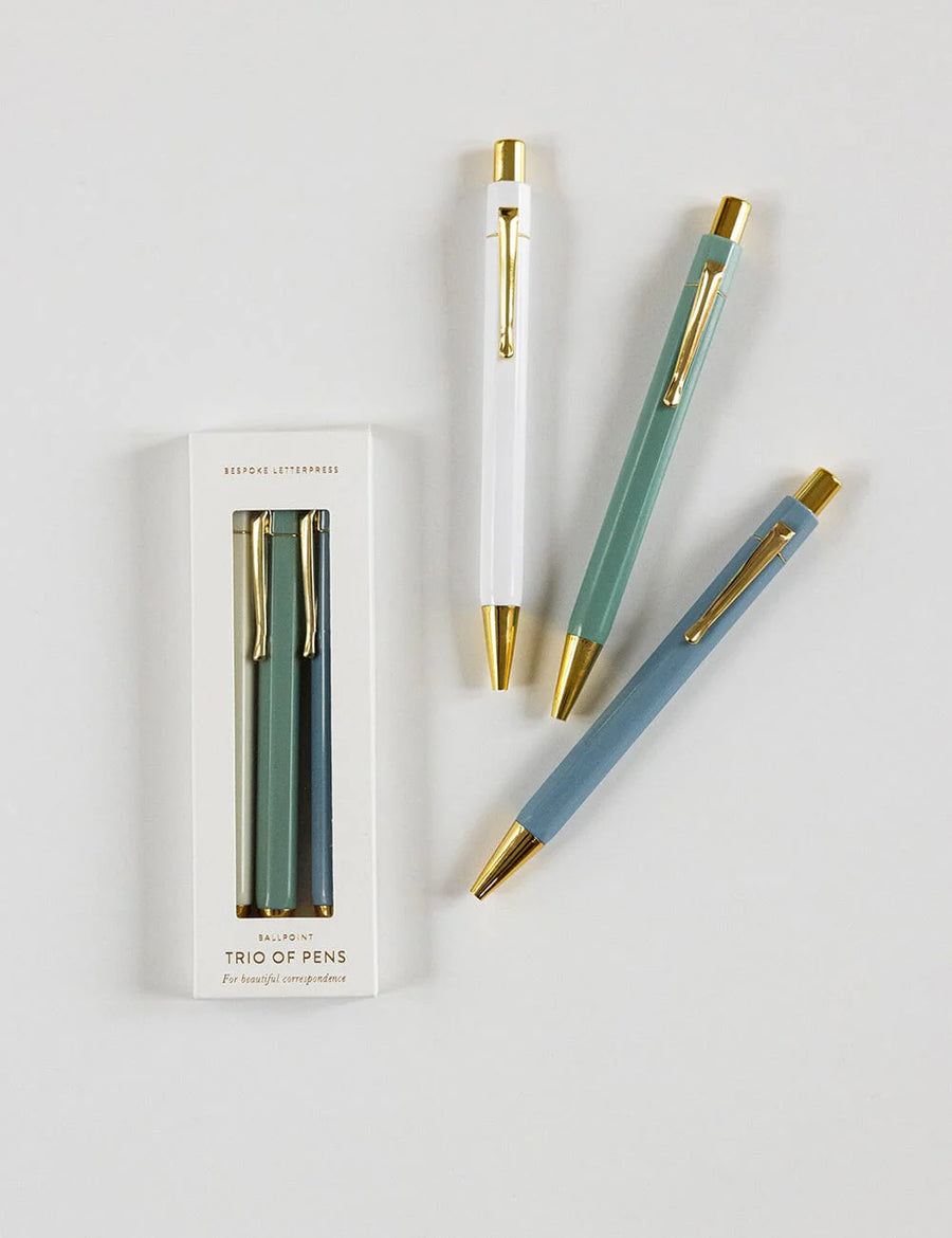 Set of three pens with gold accents and packaging on a light gray background