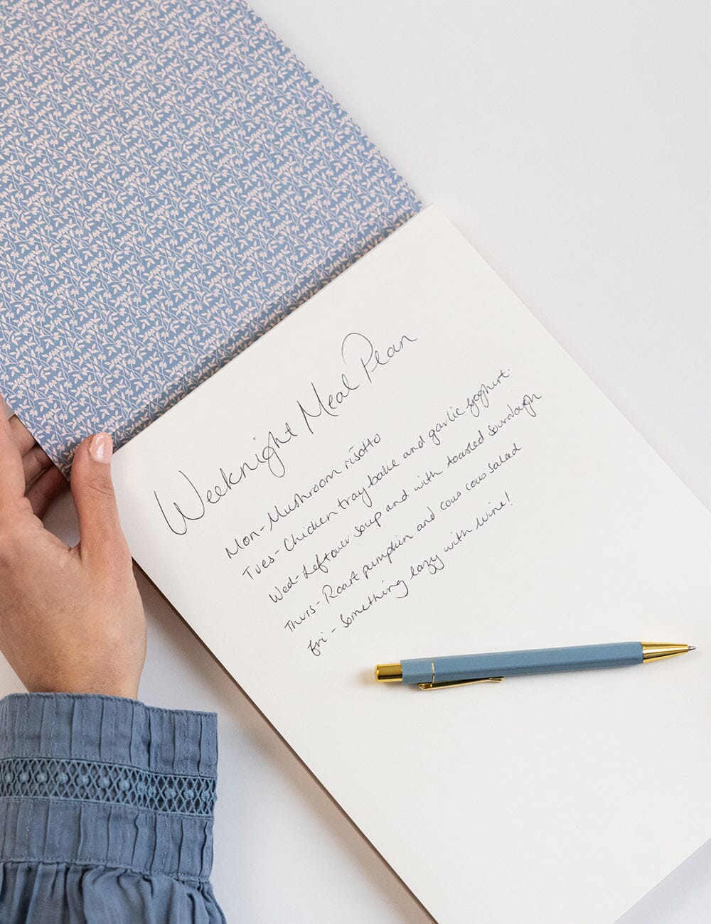 Handwritten weekly meal plan on a notebook with a pen and fabric swatch.