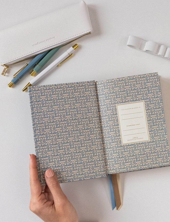 Hand holding a patterned notebook with stationery items on a light surface