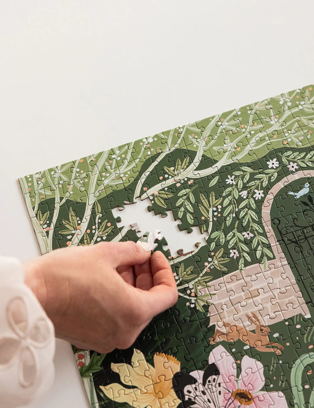 Hand placing a puzzle piece on a green-themed puzzle with floral and nature design.