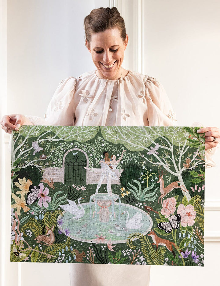 Woman holding a complete puzzle of a garden scene with people and animals.