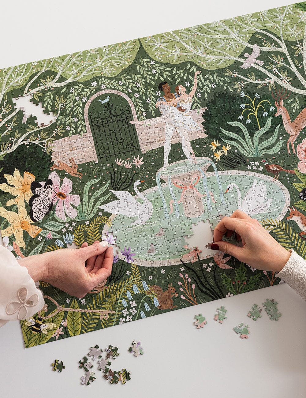 Person assembling a puzzle with a fantasy garden design on a green mat.
