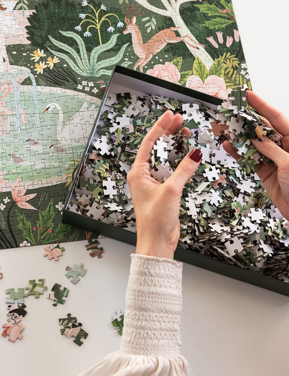 Person holding a partially completed puzzle with a forest design on a white surface