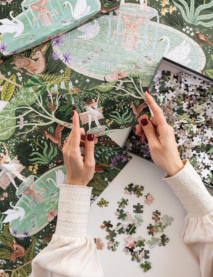 Person assembling a puzzle with a fantasy design featuring fairies and swans.
