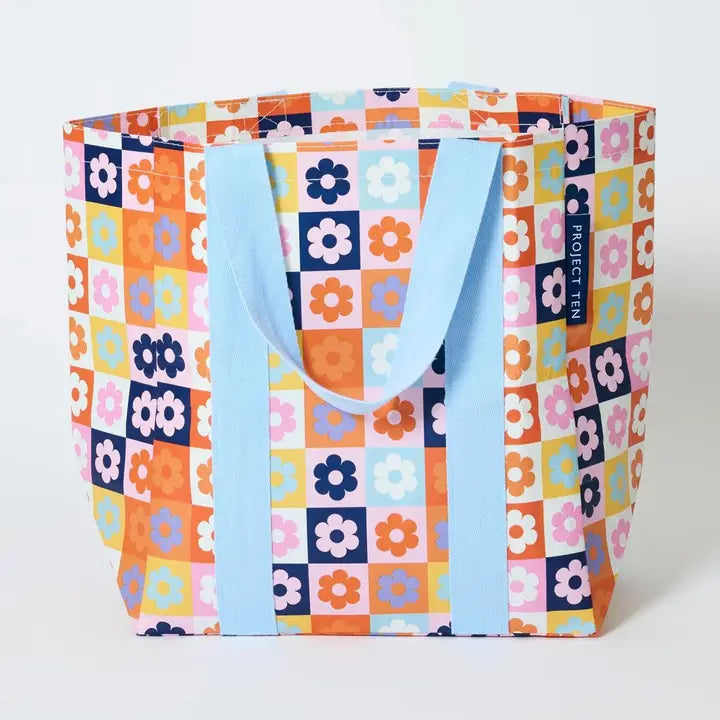 Colorful tote bag with floral pattern and blue handles on a white background