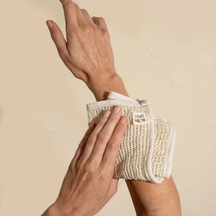 Person using a white exfoliating glove on their arm against a beige background