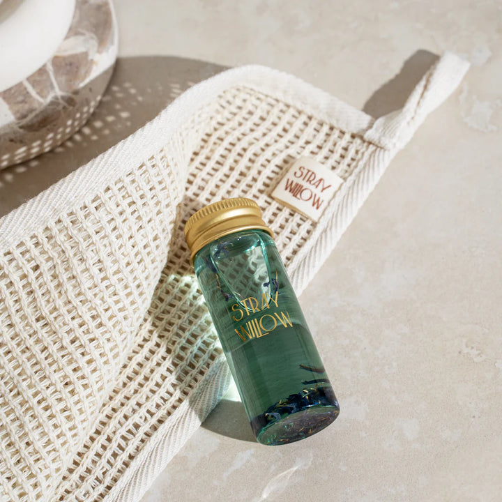 Green bottle with gold cap on a woven mat with 'Stray Willow' branding