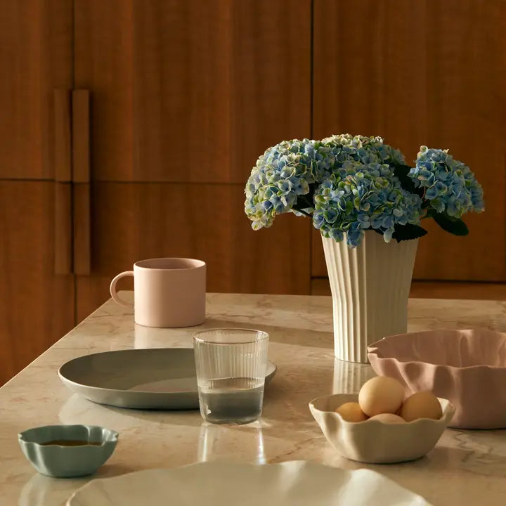 Table setting with a vase of flowers, cups, and bowls on a wooden surface.
