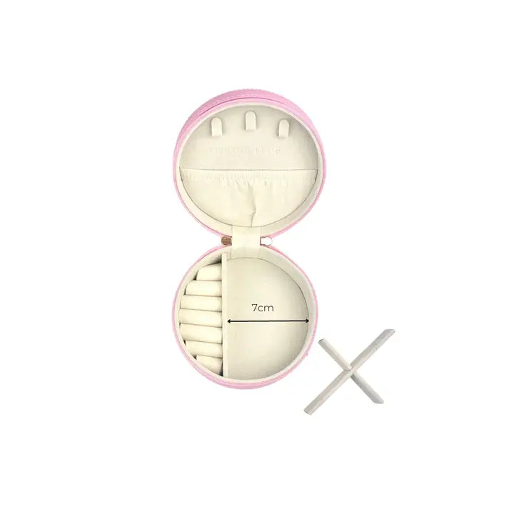 An open round pink jewelry organizer case with cream-colored compartments and a 7cm width measurement printed on the inside, shown alongside a white cross-shaped stand on a plain white background.