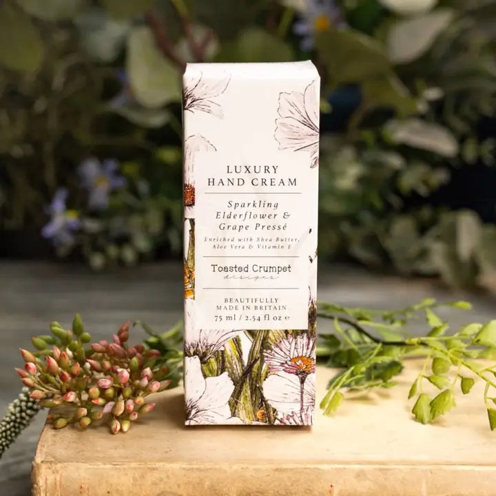Box of luxury hand cream with botanical design on a wooden surface with plants in the background