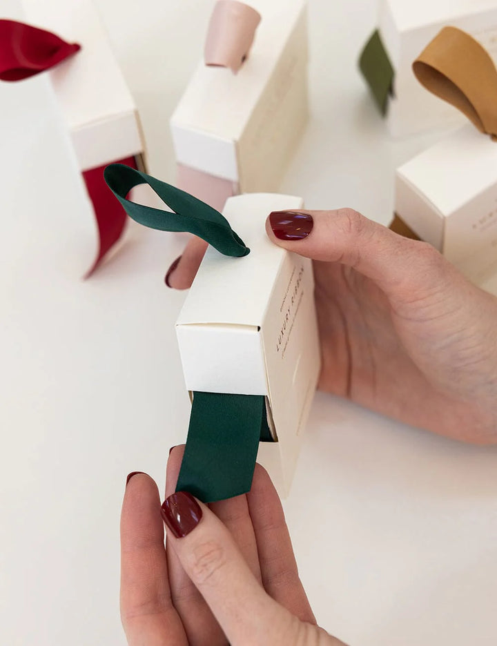 Person holding a white box with a green ribbon against a neutral background