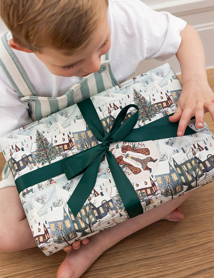 Child holding a wrapped gift with festive christmas design and green ribbon
