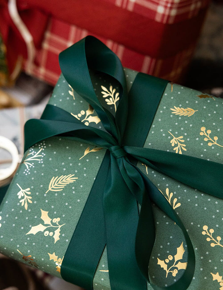 Green gift box with gold patterns and a green ribbon on a blurred background