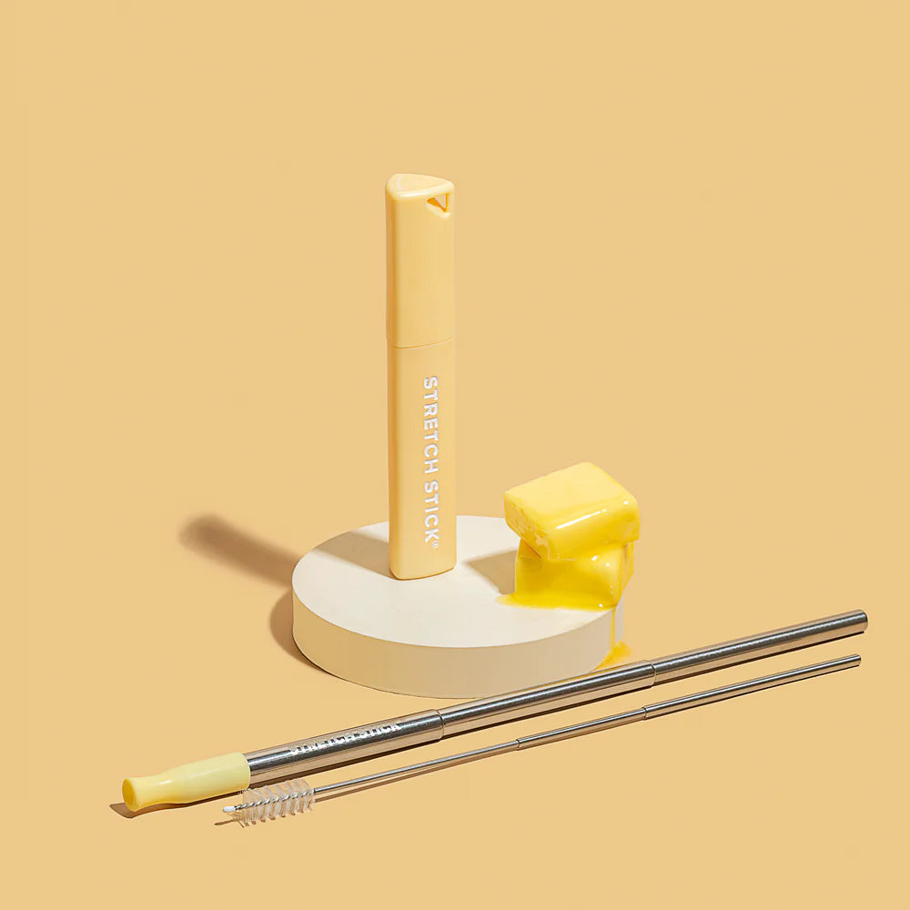 Yellow Stretch Stick case with pieces of butter, stainless steel straw & cleaning brush on a yellow background