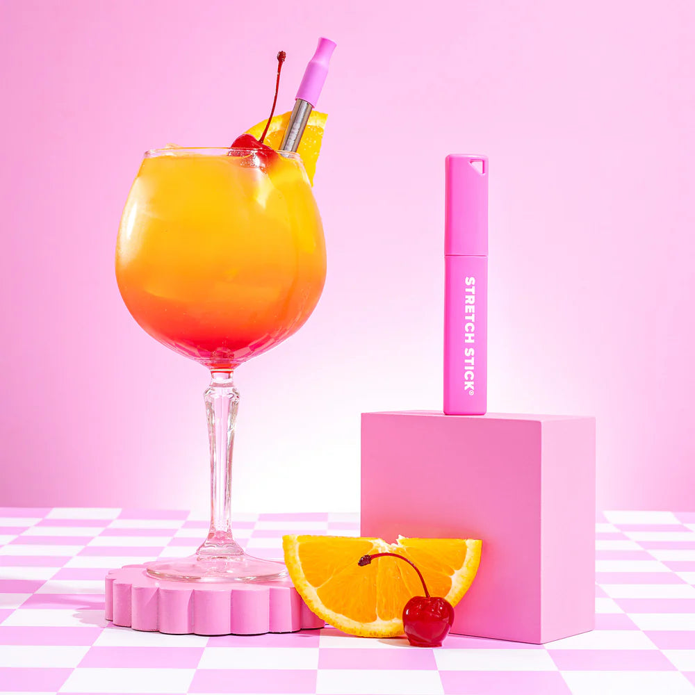Stretch stick cover on a pink box with a stainless steel reusable straw in a cocktail on a pink and white check surface and pink background