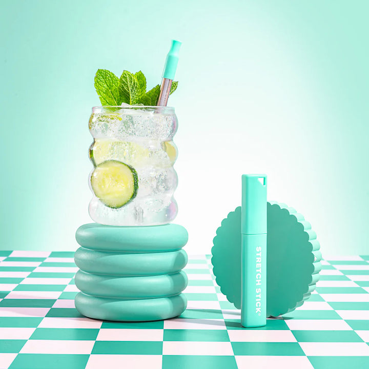 Reusable stretch stick case and a glass with a stainless steel straw on a check surface and green background