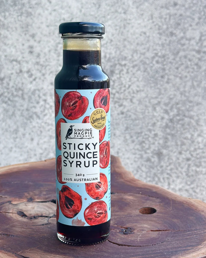 Bottle of Sticky Quince Syrup on a wooden surface with a textured gray background