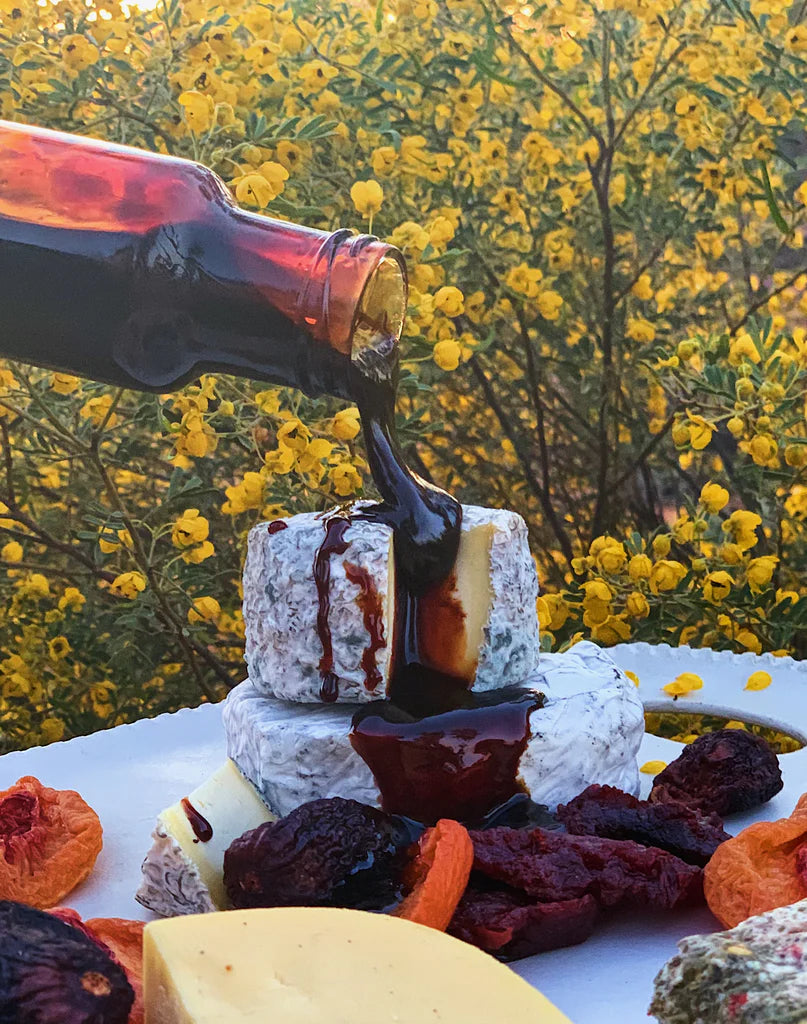 Bottle pouring sticky quince syrup over cheese and dried fruits with a natural background