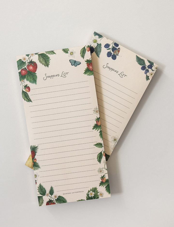 Two notepads with floral and fruit designs on a light gray background